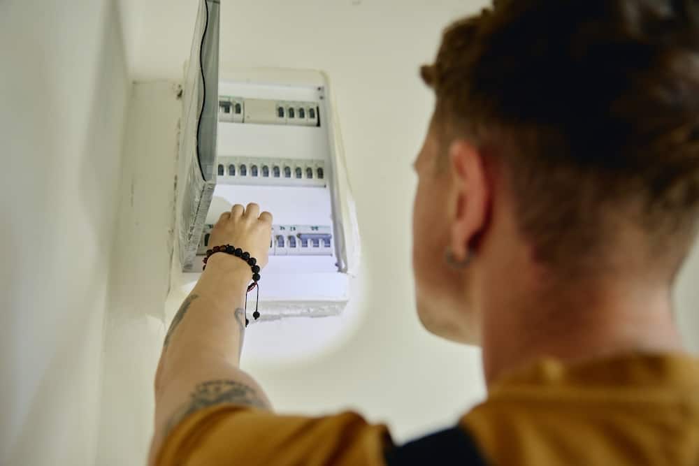 Electrical Panel Inspection Guide 3 A man reaches up to check a wall-mounted breaker box during a home electrical panel inspection.