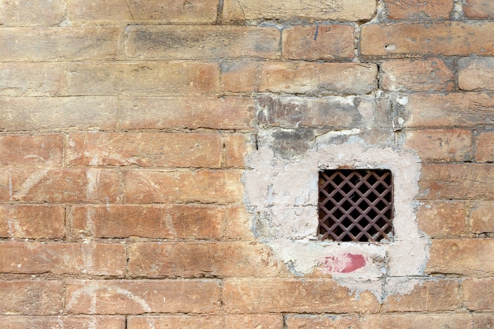 What Is a Weep Hole? A Home Inspector's Guide 3 A square lattice vent set into a weathered brick wall helps answer what is a weep hole and how wall ventilation works.