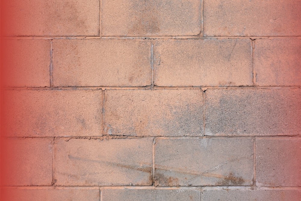What Is a Weep Hole? A Home Inspector's Guide 1 A close-up view of a weathered, peach-tinted concrete block wall with visible mortar joints and light surface staining.